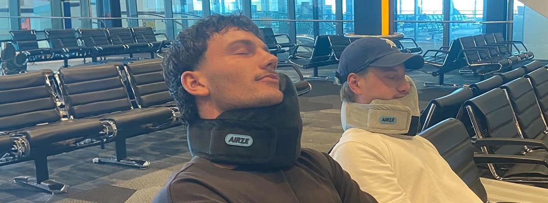 Two men resting in an airport lounge using Airze travel pillows in black and grey, demonstrating neck support and travel comfort while waiting for their flight.