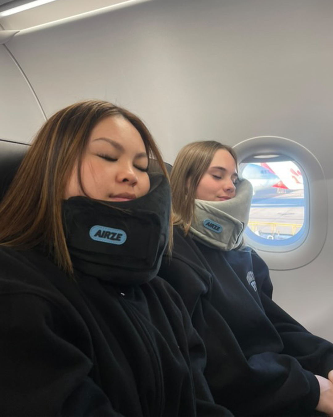 Two women sleeping comfortably on an airplane using Airze travel pillows in black and grey, designed for superior neck support during flights.
