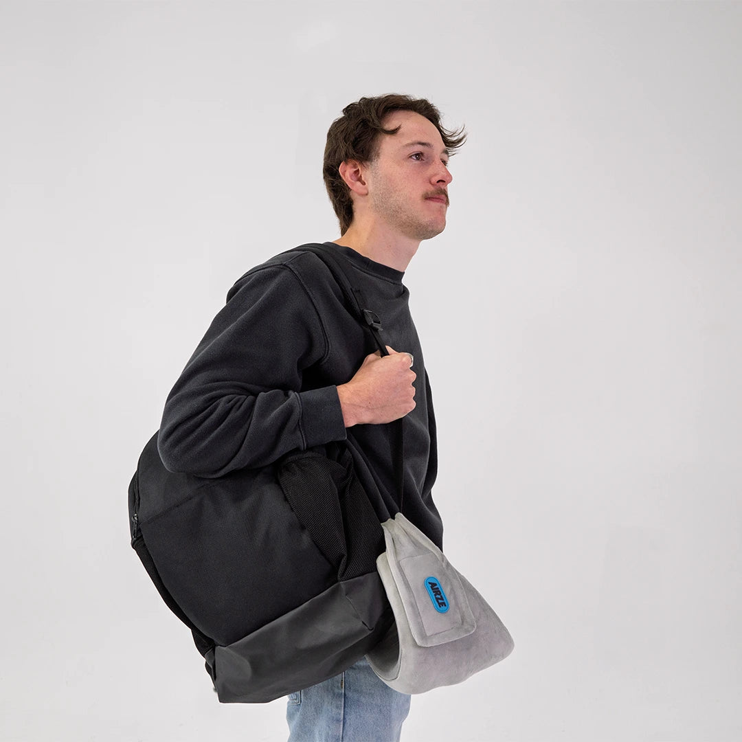 Traveler carrying the Airze travel pillow in grey, conveniently attached to a backpack for easy portability and hands-free travel comfort.