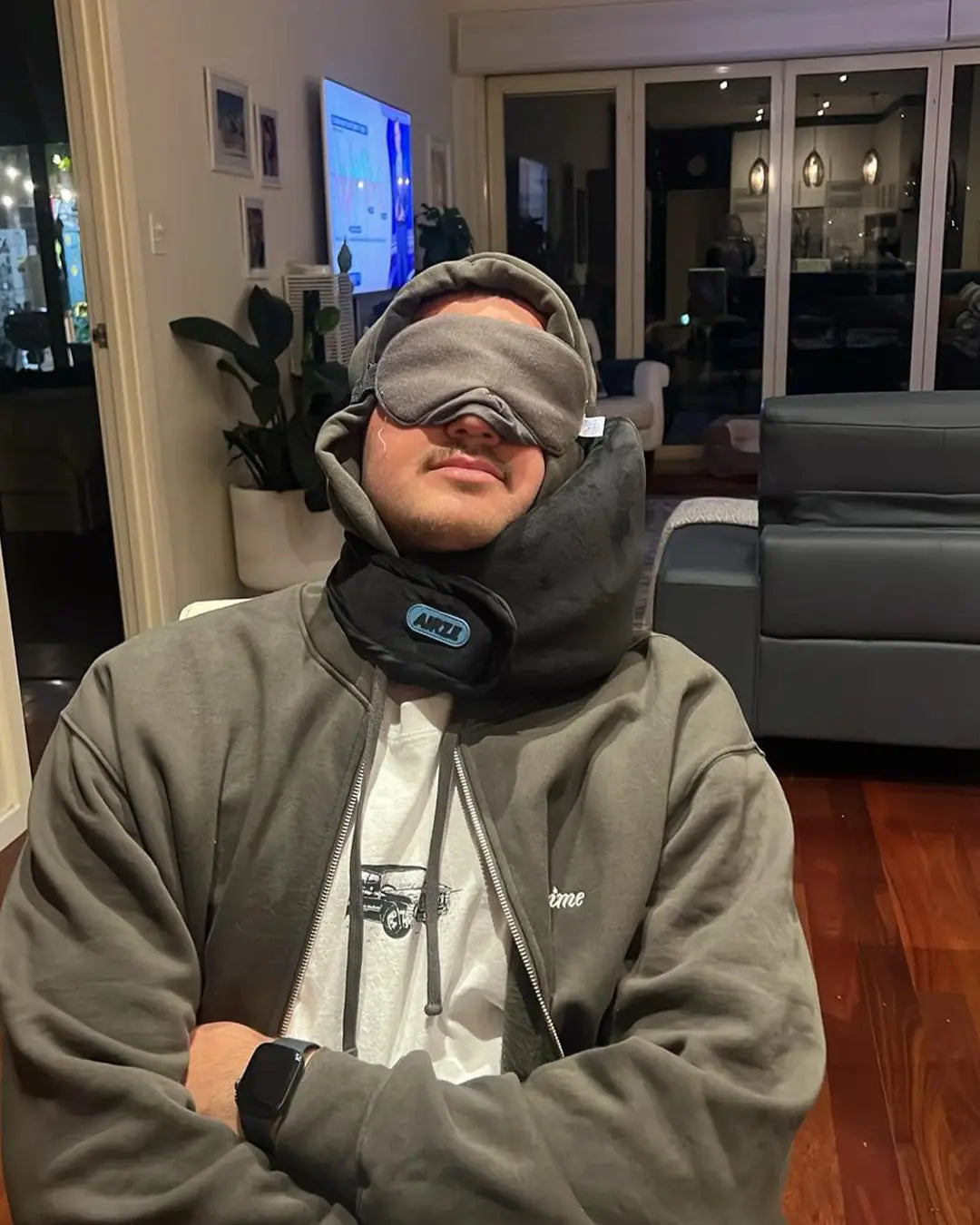 Man resting at home using a black Airze travel pillow for neck support and relaxation.